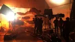 A film crew in a studio is setting up a shot of a large screen with floating grey and orange cut-out clouds.